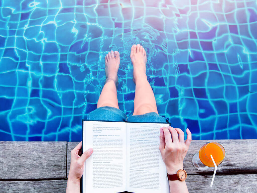 man sitting on the side of pool with his legs in the water and a book in his hands